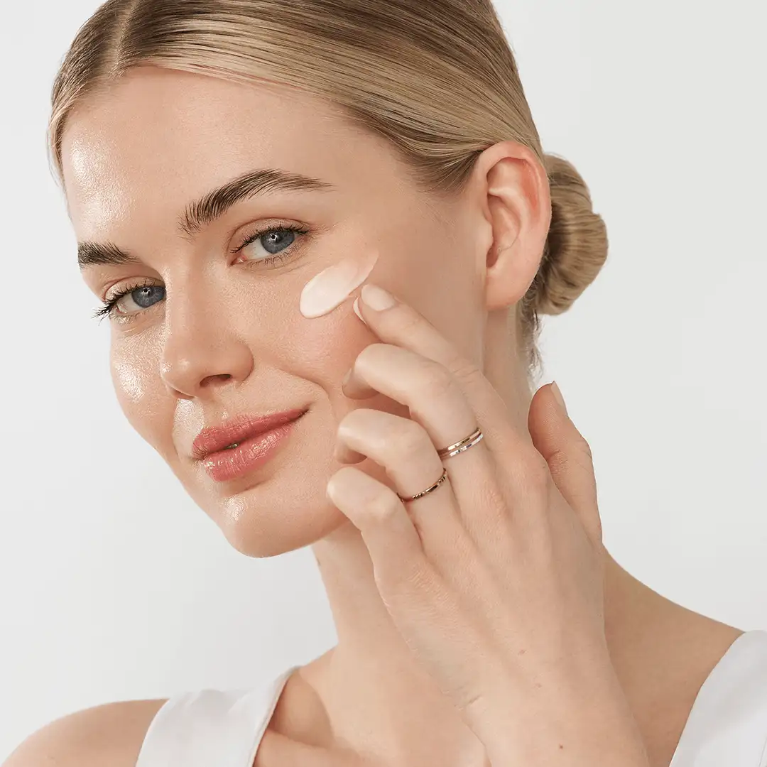 Frau trägt SUPREME GLOW CREAM GEL von ANNEMARIE BÖRLIND auf die Wange auf, helle Hautpflege