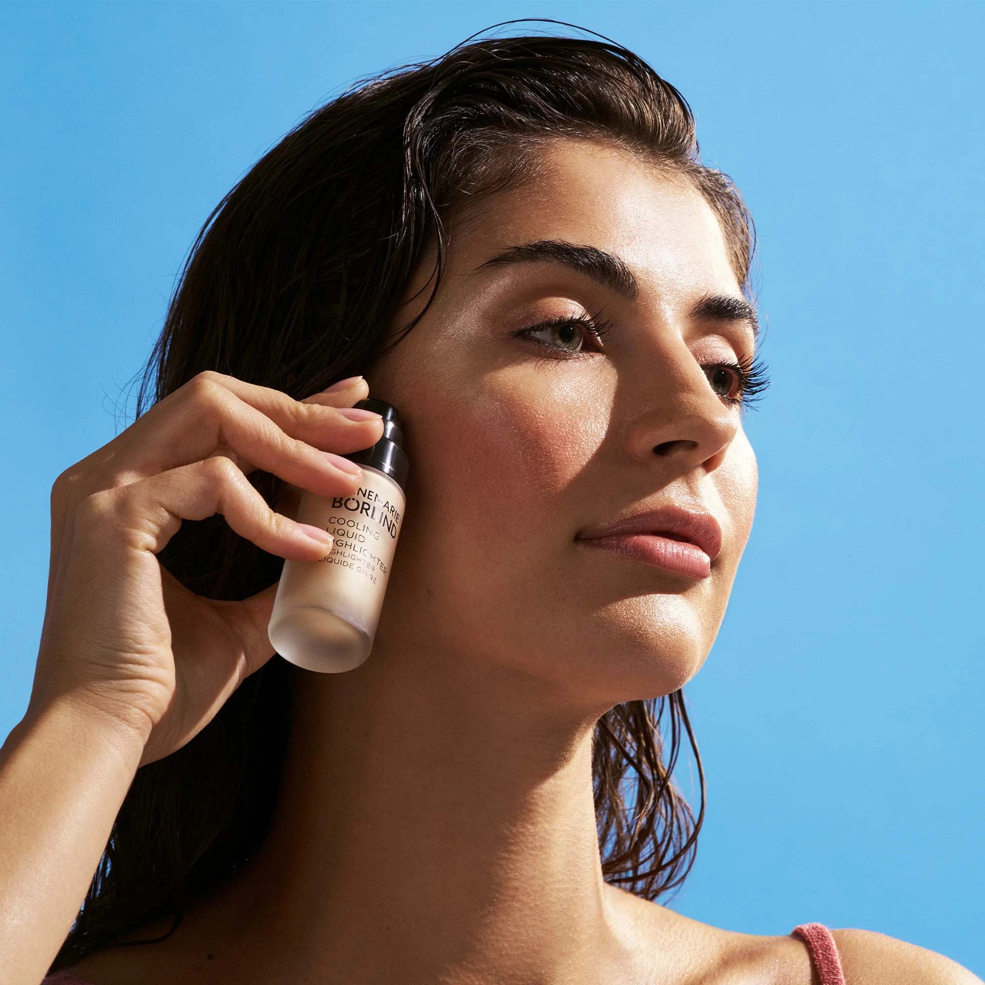 Frau hält ANNEMARIE BÖRLIND Cooling Liquid Highlighter nahe Gesicht vor blauem Himmel