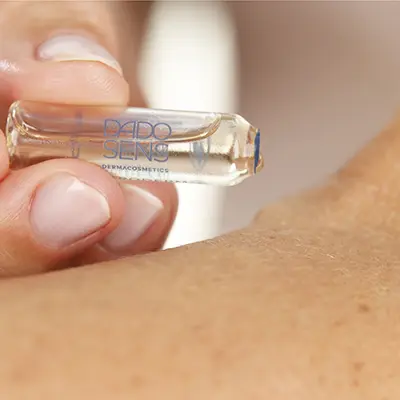 DADO SENS Ampulle mit klarem Serum wird auf die Haut am Schulterbereich aufgetragen