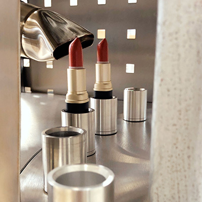 Zwei rote Lippenstifte in silbernen Hüllen werden mit einer Flamme geformt, Produktionsprozess sichtbar