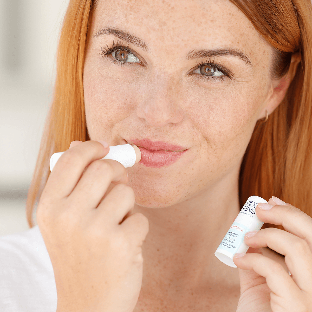 Frau trägt DADO SENS LIPCARE Intensiv-Lipbalm auf ihre Lippen auf, Nahaufnahme Gesicht und Hände