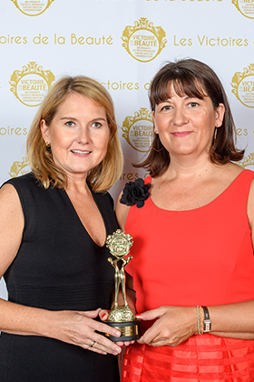Zwei Frauen in schwarzem und rotem Kleid halten gemeinsam eine goldene Trophäe vor weißem Hintergrund mit Logos