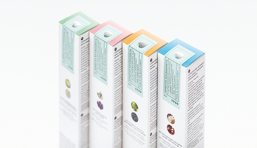 Vier schmale Produktverpackungen mit farbigen Deckeln in Grün, Rosa, Orange und Blau, Text und kleinen Bildern auf Weiß