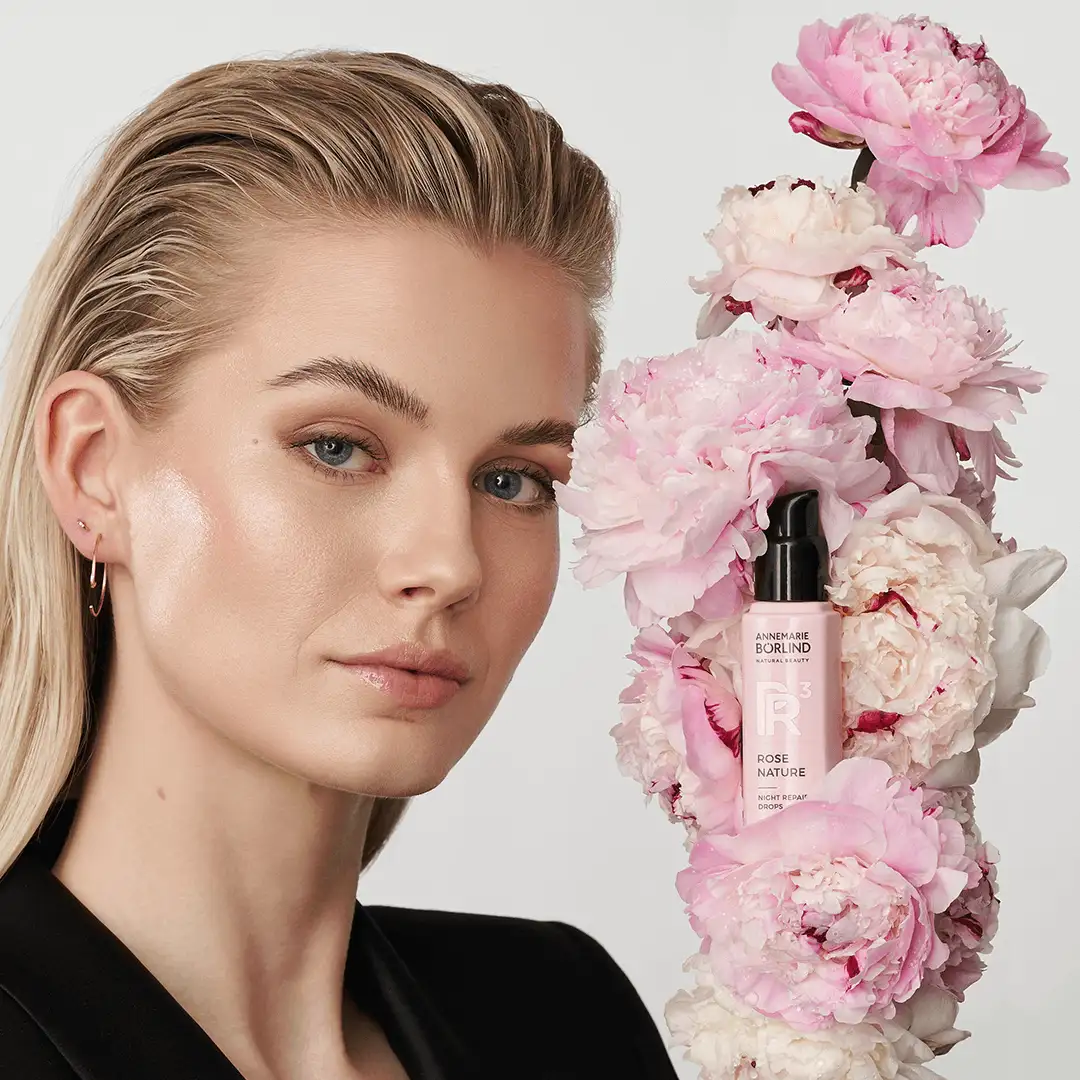 Frau mit glatter Haut neben ANNEMARIE BÖRLIND ROSE NATURE Night Repair Drops umgeben von rosa Pfingstrosen