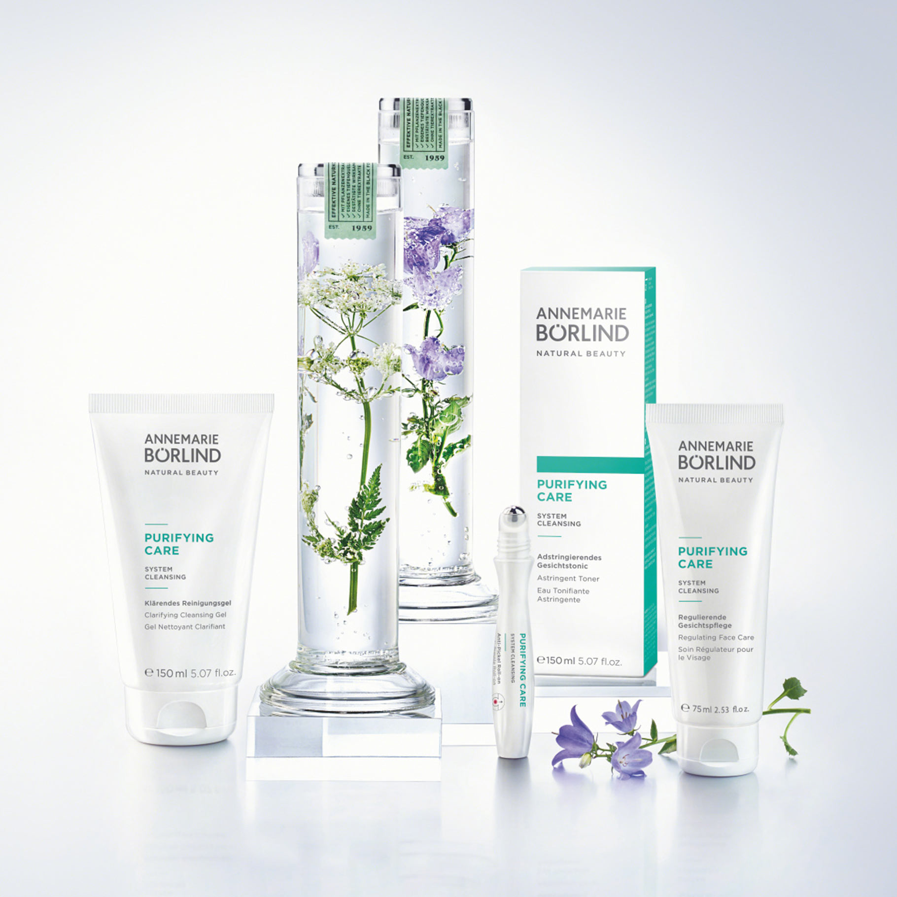 ANNEMARIE BÖRLIND PURIFYING CARE Reinigungs- und Pflegeprodukte mit Pflanzen in Glaszylindern und lila Blüten