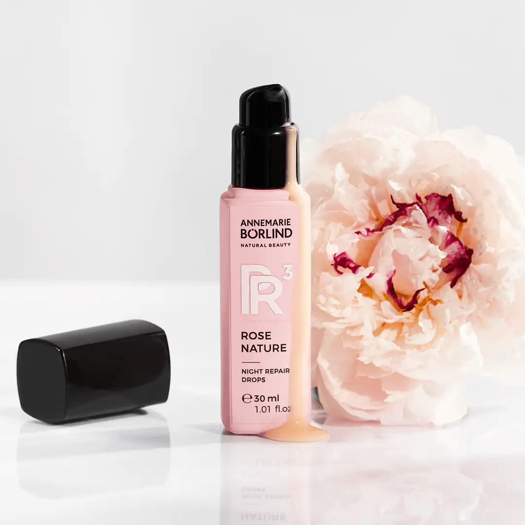 ANNEMARIE BÖRLIND ROSE NATURE Night Repair Drops 30 ml mit Serum vor hellrosa Blüte auf weißem Untergrund