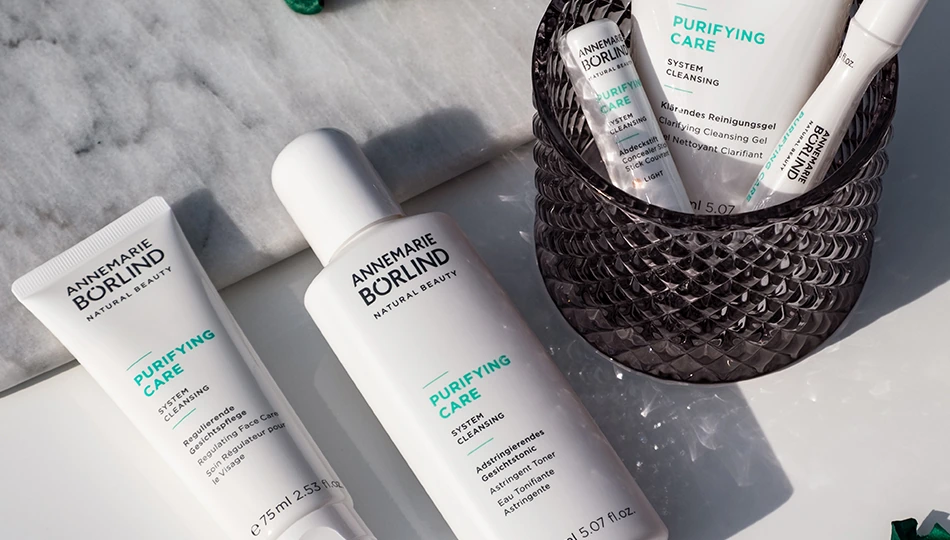 Produkte der ANNEMARIE BÖRLIND PURIFYING Care Serie auf Marmoruntergrund: Gesichtspflege und Gesichtstonic liegend, daneben im Glas Abdeckstift, Reinigungsgel und Anti-Pickel Roll-on.