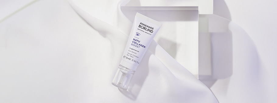 ANNEMARIE BÖRLIND NATU COLLAGEN BOOST Augenserum in weißer Tube auf weißem Stoff und geometrischem Hintergrund