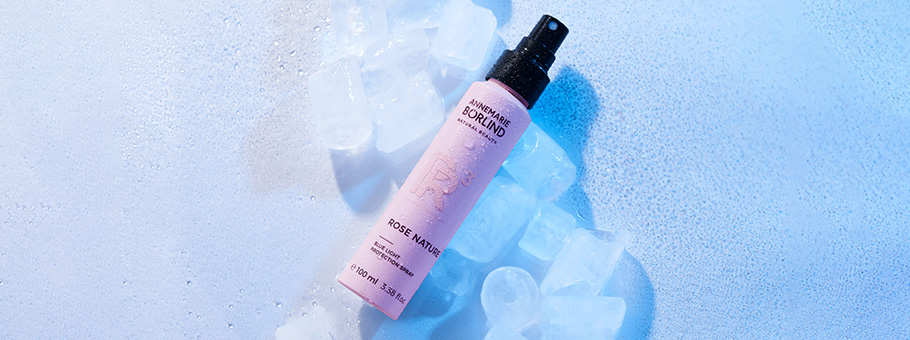 ANNEMARIE BÖRLIND ROSE NATURE Blue Light Protection Spray auf Eiswürfeln vor blauem Hintergrund
