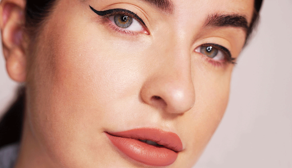 Nahaufnahme eines Gesichts mit betontem schwarzem Eyeliner und mattem, roten Lippenstift, glatte Haut
