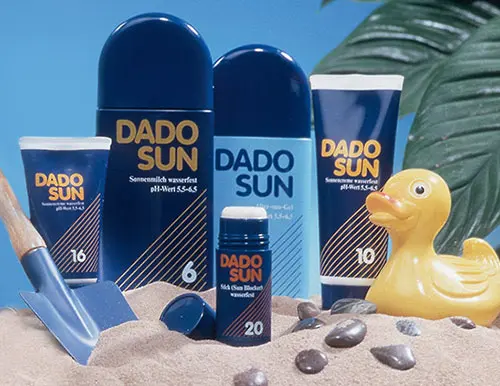 DADO SUN Sonnencremes mit LSF 6, 10, 16, 20 in Sand mit gelbem Quietscheentchen und blauem Sandspielzeug