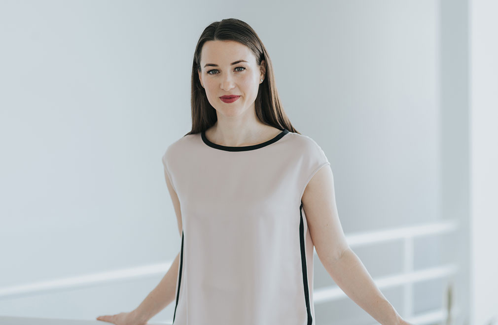 Frau steht lächelnd an hellem Geländer in modernem, minimalistischem Innenraum