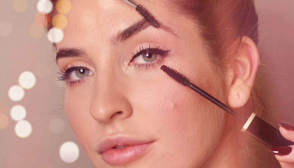 Nahaufnahme einer Frau, die Mascara auf die oberen Wimpern aufträgt, mit weichem Licht und Bokeh-Effekt