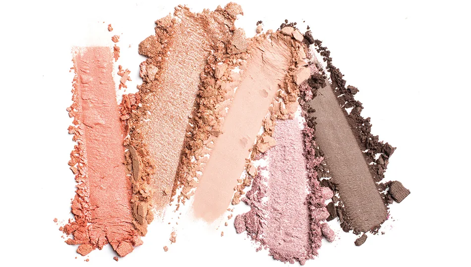 Verschiedene Lidschattenfarben in pudriger Textur – von Rosé über Gold und Taupe bis Dunkelbraun – nebeneinander aufgetragen und teils zerbröselt.