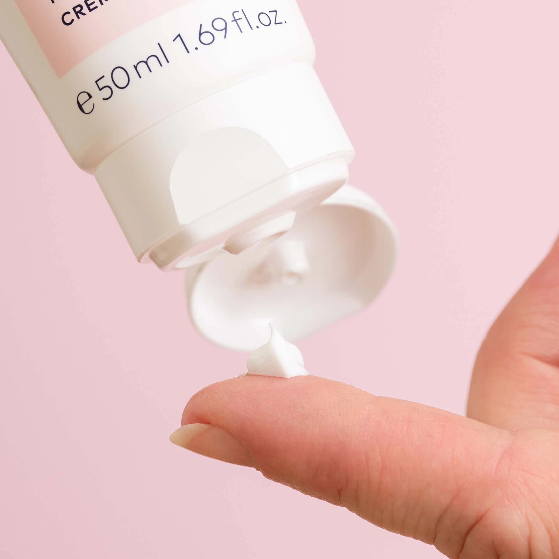 DADO SENS EXTRODERM Intensivcreme-Textur auf Finger vor rosa Hintergrund, Tube mit 50 ml Inhalt