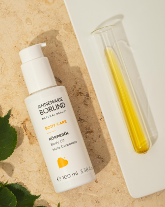 ANNEMARIE BÖRLIND BODY CARE Körperöl in weißer Flasche neben Reagenzglas mit gelbem Öl auf hellem Untergrund