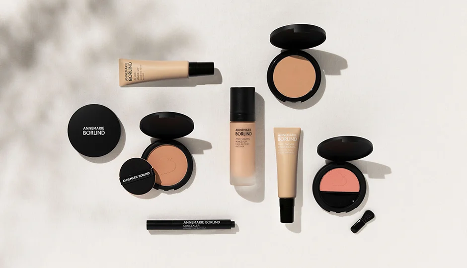 ANNEMARIE BÖRLIND Make-up-Sortiment mit Foundation, Puder, Concealer und Rouge in schwarzen Verpackungen auf hellem Hinter...