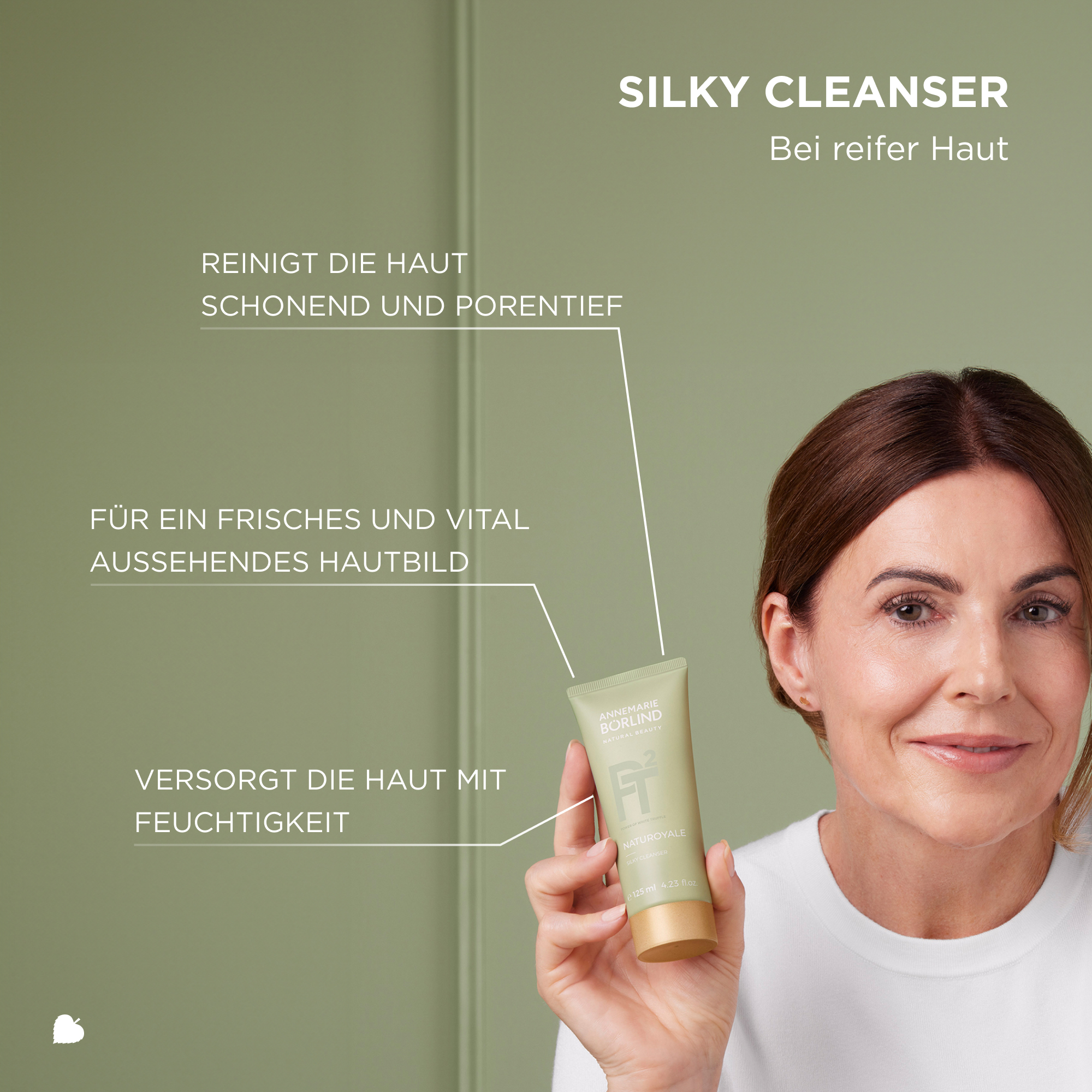 Frau hält ANNEMARIE BÖRLIND NATUROYALE Silky Cleanser für reife Haut vor grünem Hintergrund