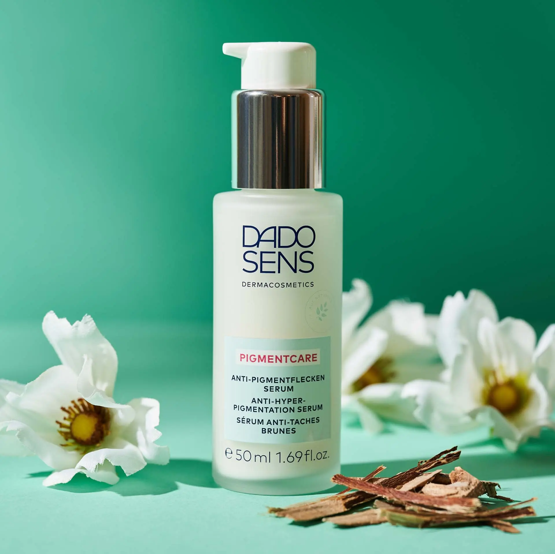 DADO SENS Pigmentcare Anti-Pigmentflecken Serum 50 ml mit weißen Blüten und Holzstücken auf grünem Hintergrund