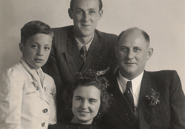 Vier Personen in formeller Kleidung, zwei Männer, ein Junge und eine Frau mit Blumenschmuck, Gruppenporträt in Schwarz-Weiß