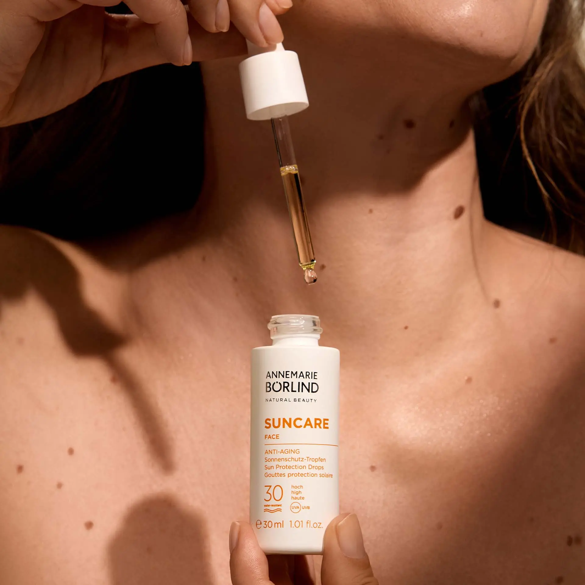 ANNEMARIE BÖRLIND Suncare Anti-Aging Sonnenschutz-Tropfen SPF 30 für das Gesicht, 30 ml mit Pipette und Model im Hintergrund