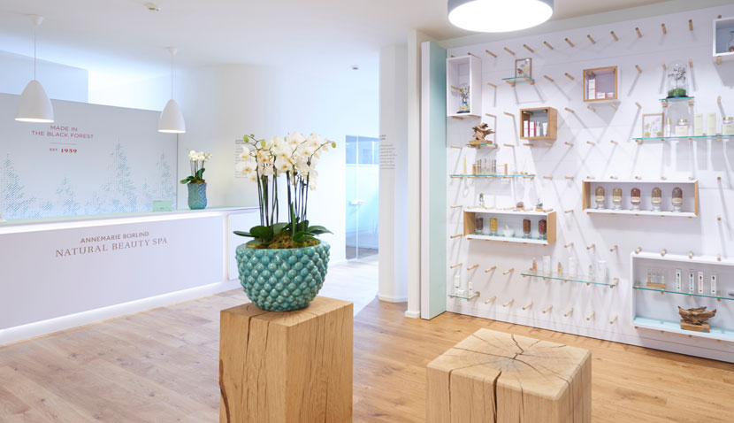 Empfangsbereich des ANNEMARIE BÖRLIND NATURAL BEAUTY SPA mit Holzsäulen, Orchideen und Produktregal an weißer Wand